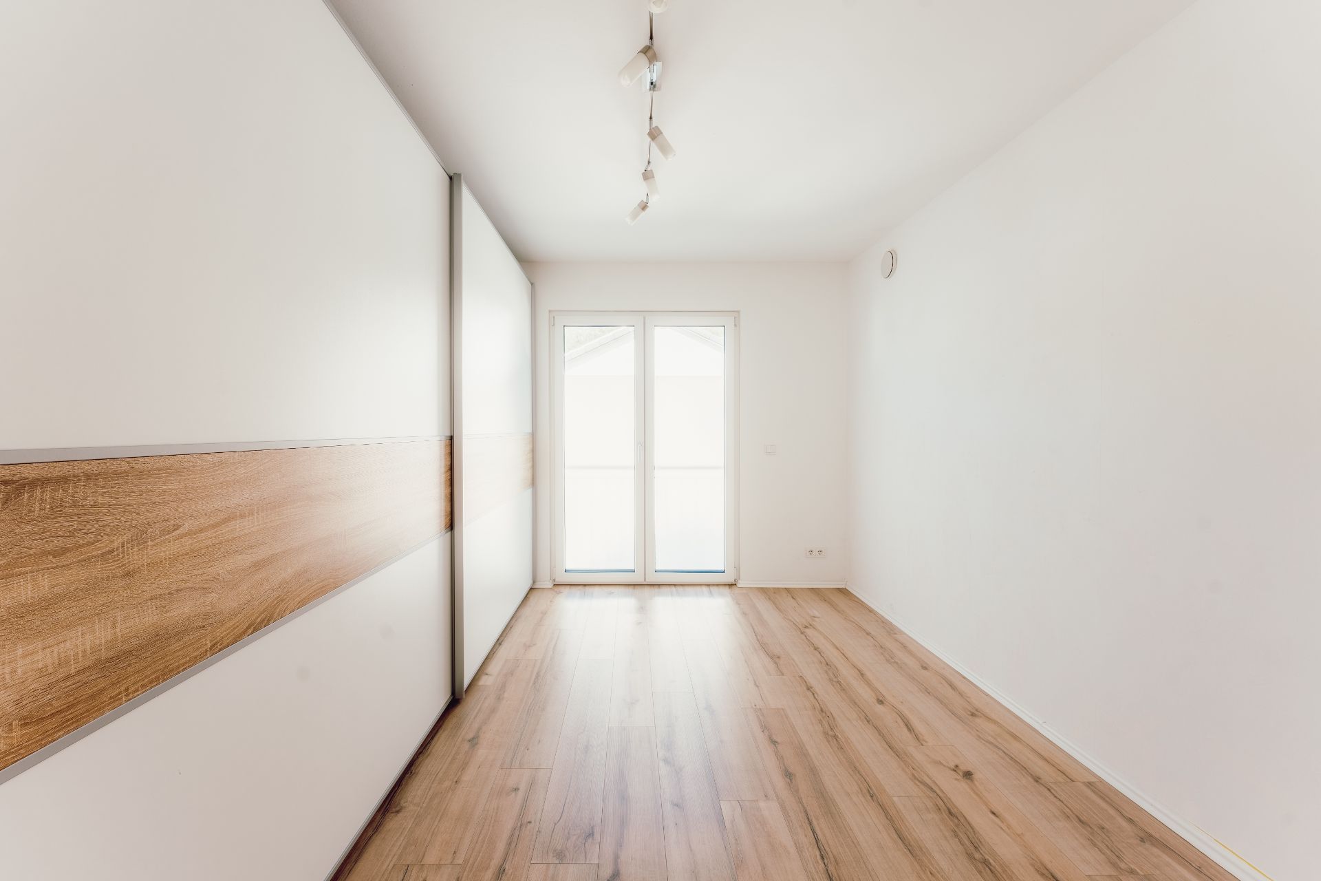 Leerer Raum mit Holzboden, Einbauschrank und großer Tür zum Balkon.