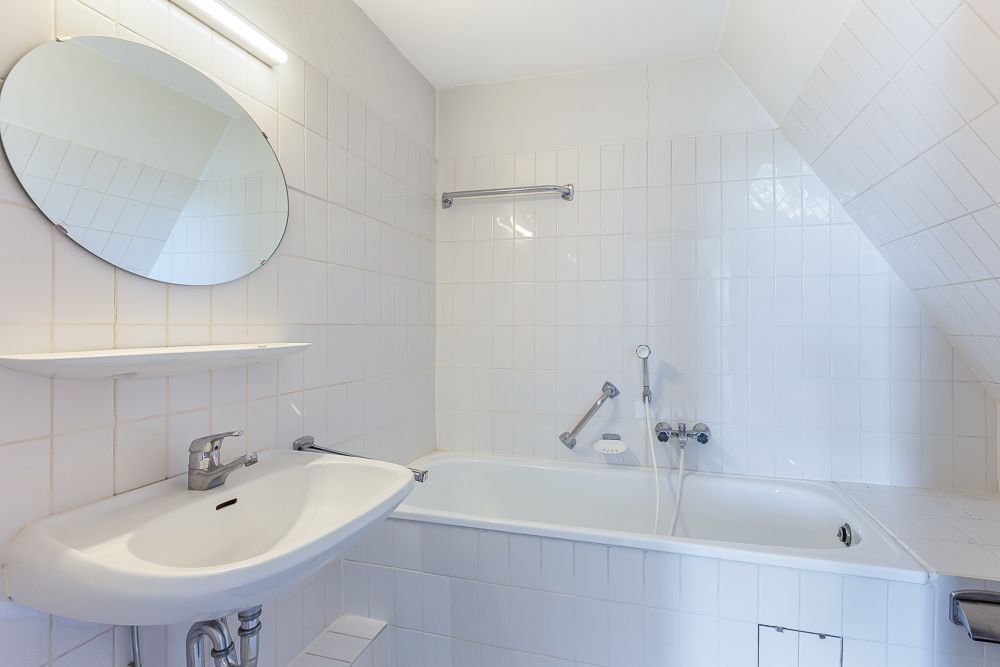 Weiß gefliestes Badezimmer mit Waschbecken, Spiegel und Badewanne.