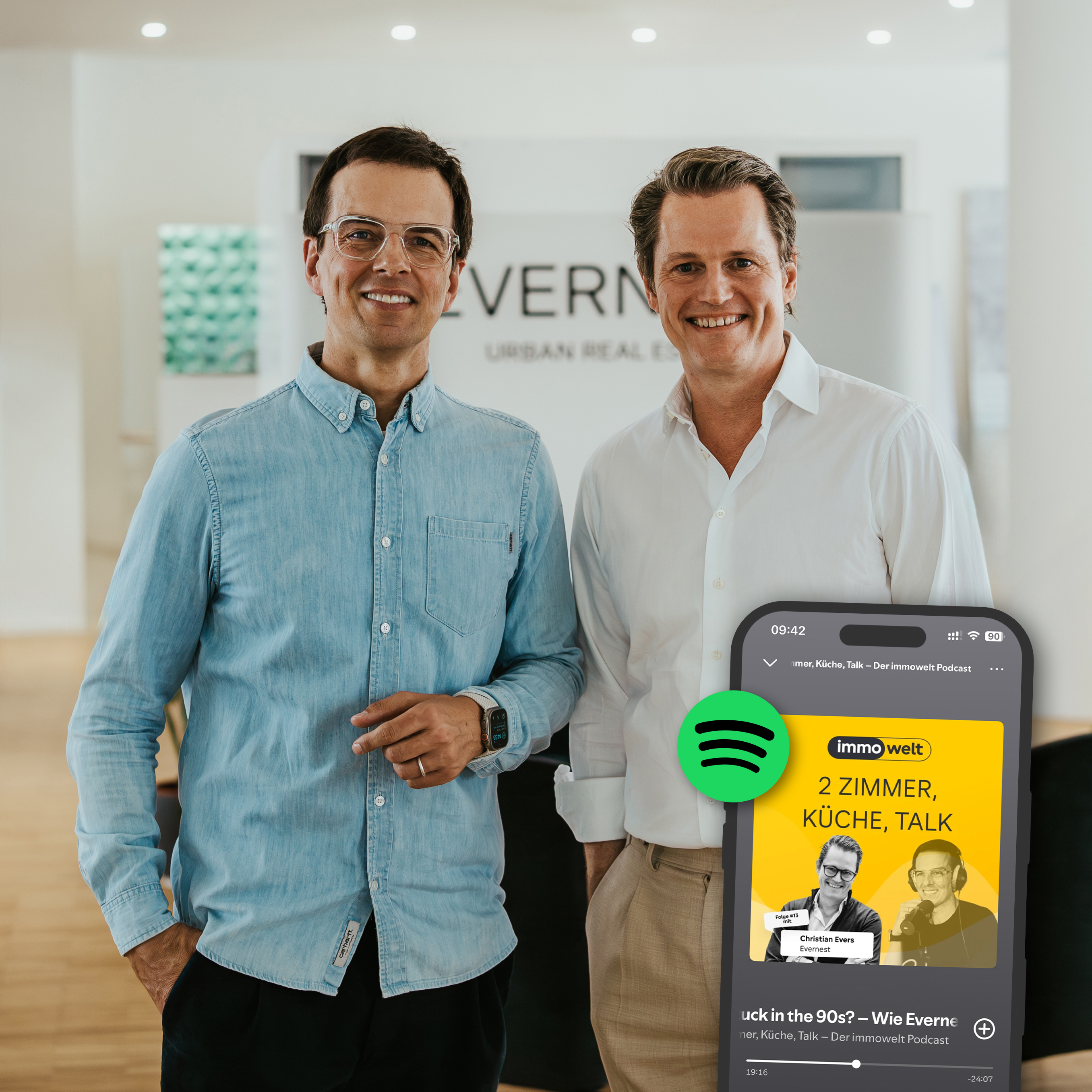 Zwei Männer stehen in einem modernen, hellen Raum. Im Vordergrund ist ein Smartphone mit Podcast-Anzeige zu sehen.