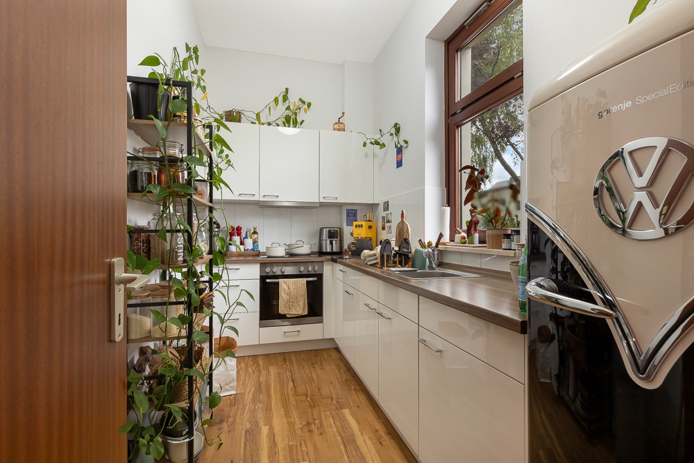 Moderne Küche mit weißen Schränken, Holzboden, Pflanzen und großem Fenster.