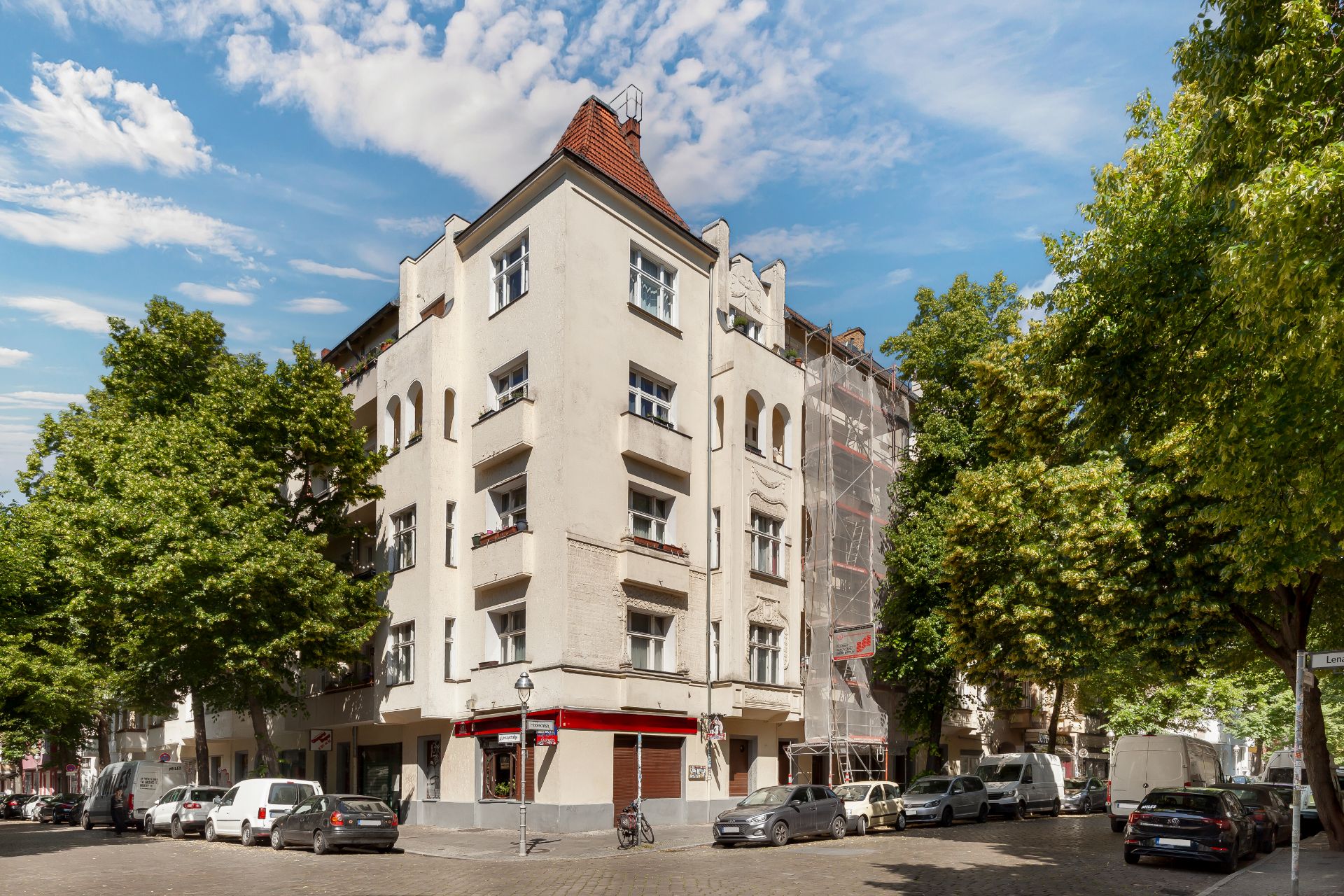 Eckwohnhaus mit weißen Fassaden, roten Dachziegeln und parkenden Autos an der Straße.