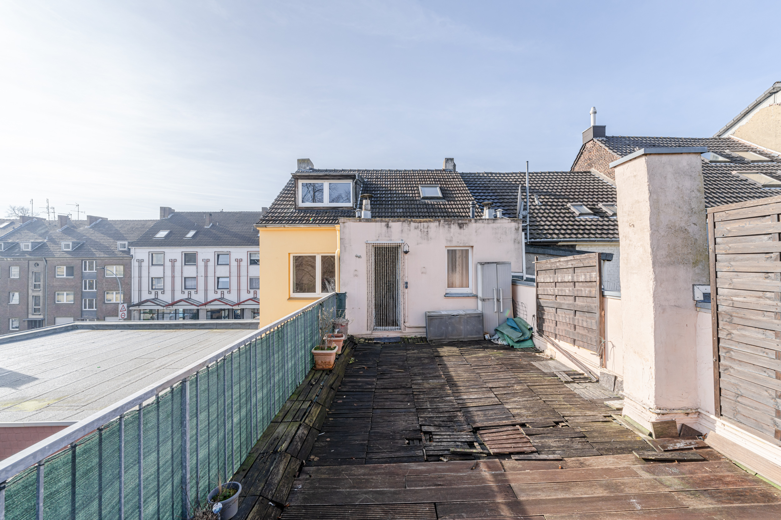 Dachterrasse mit Holzboden, Blumenkästen und Blick auf angrenzende Wohnhäuser.