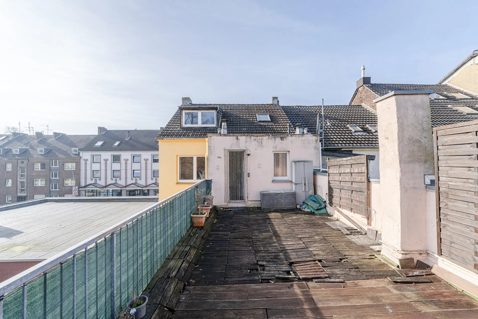 Dachterrasse mit Holzboden, Blumenkästen und Blick auf angrenzende Wohnhäuser.