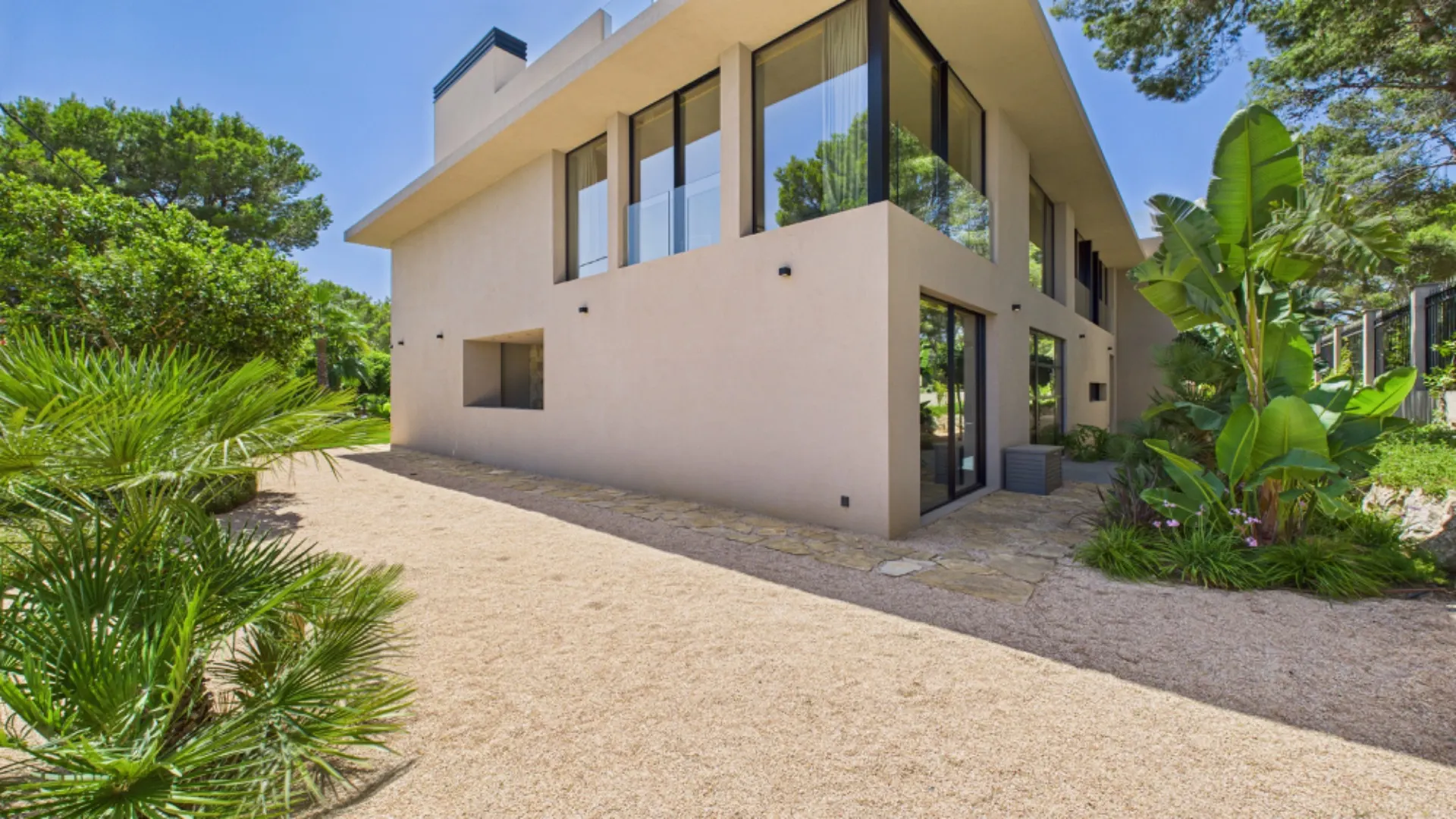Modernes, zweistöckiges Haus mit großen Fenstern, umgeben von Garten und Bäumen.