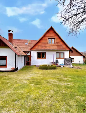 Einfamilienhaus mit Garten, rotem Dach und Terrasse, umgeben von Bäumen und Rasenfläche.
