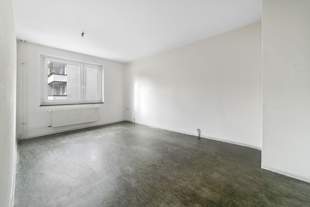 Leerer Raum mit großem Fenster, weiß gestrichenen Wänden und dunklem Boden.