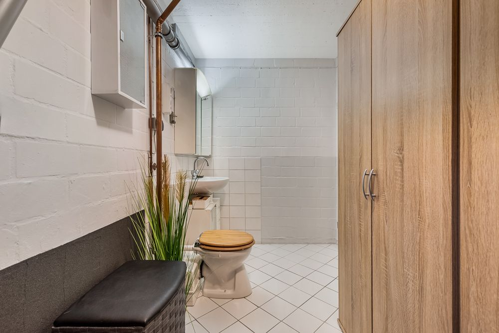 Badezimmer mit Toilette, Waschbecken, Spiegel, Holzschrank und Bank auf Fliesenboden.