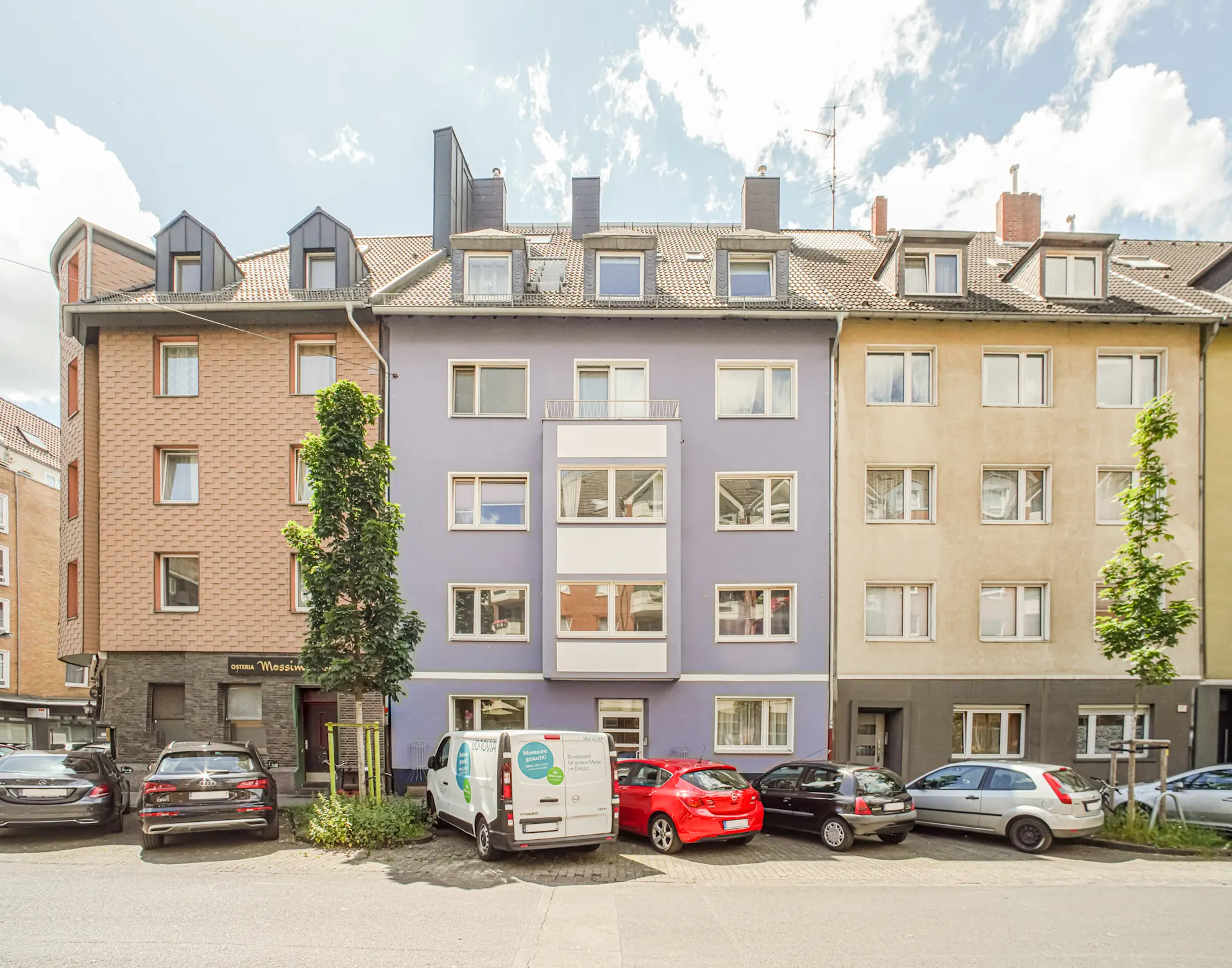 Mehrfamilienhaus mit bunter Fassade und geparkten Autos davor bei Tageslicht.