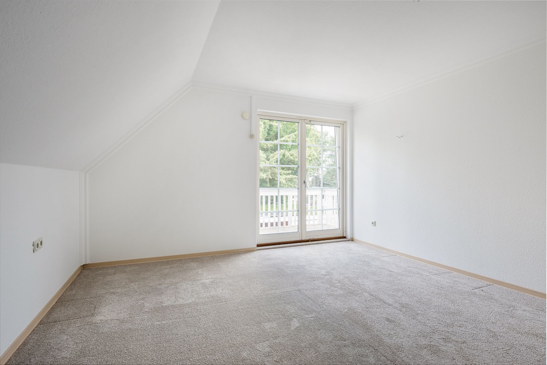 Leeres Zimmer mit Teppichboden und großen Fenstertüren zu einem Balkon.