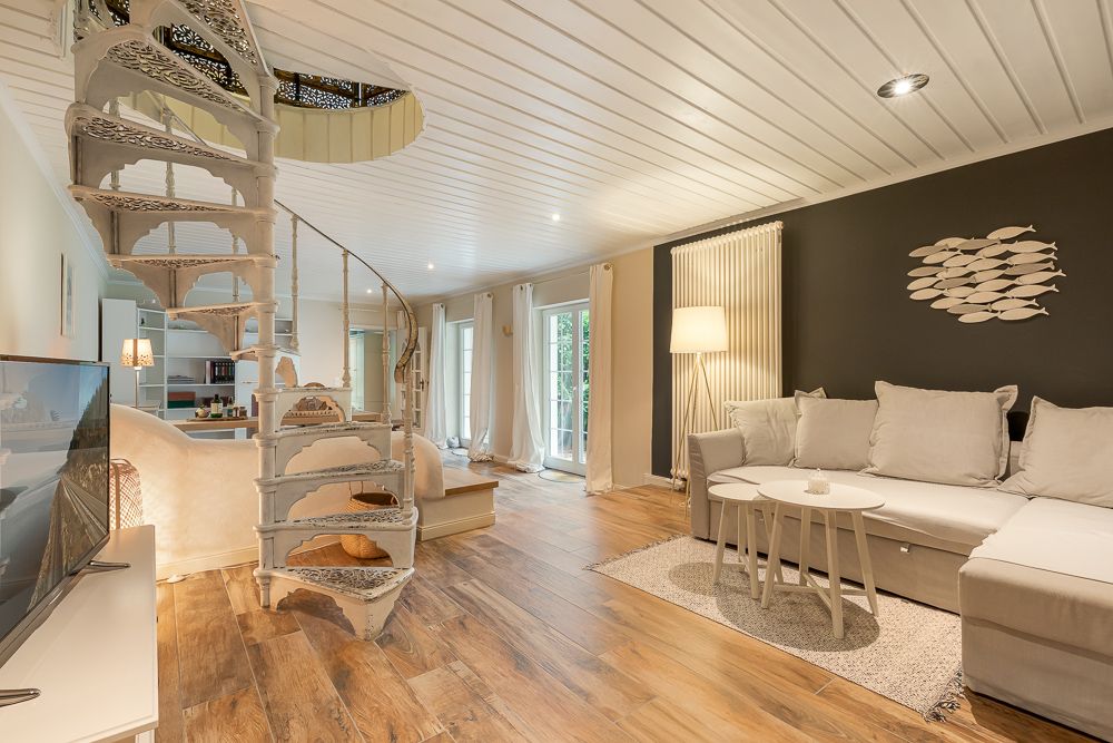 Helles Wohnzimmer mit Wendeltreppe, Sofa, TV, Stehlampe und Holzboden.