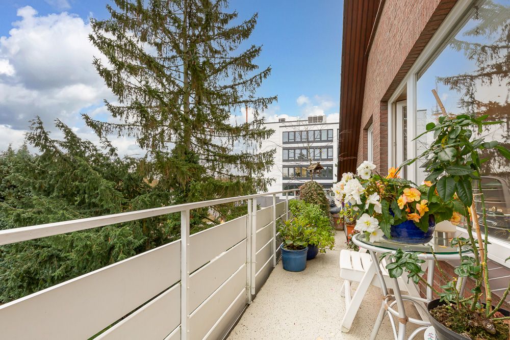 Balkon mit Topfpflanzen, kleinem Tisch und Blick auf Bäume und ein modernes Gebäude.