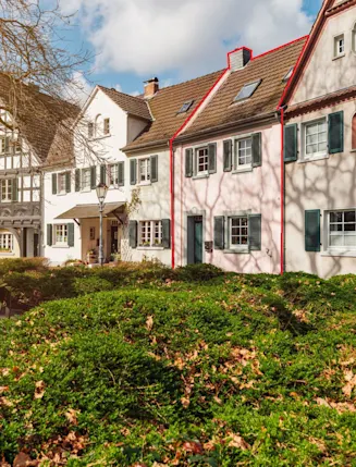 Reihenhäuser mit Vorgarten und Bänken im Vordergrund an einem sonnigen Tag.