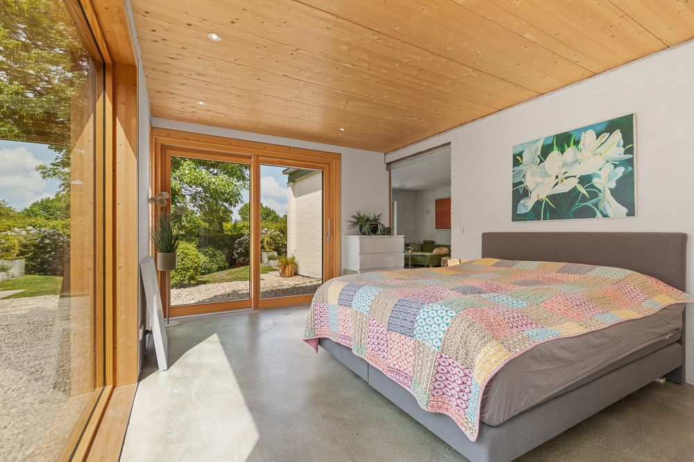 Helles Schlafzimmer mit großem Bett, buntem Bettüberwurf und Glas-Schiebetüren zum Garten.