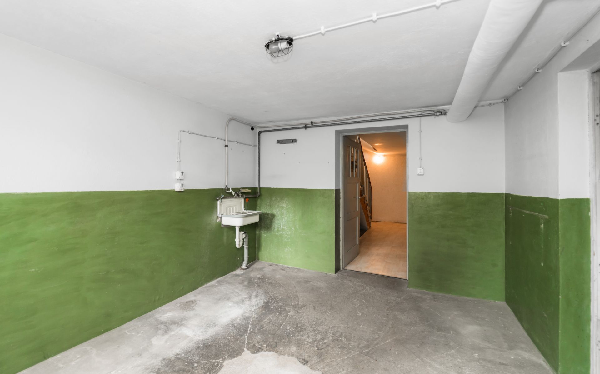 Kellerraum mit grün gestrichenen Wänden und kleinem Waschbecken, offener Durchgang zum Flur.