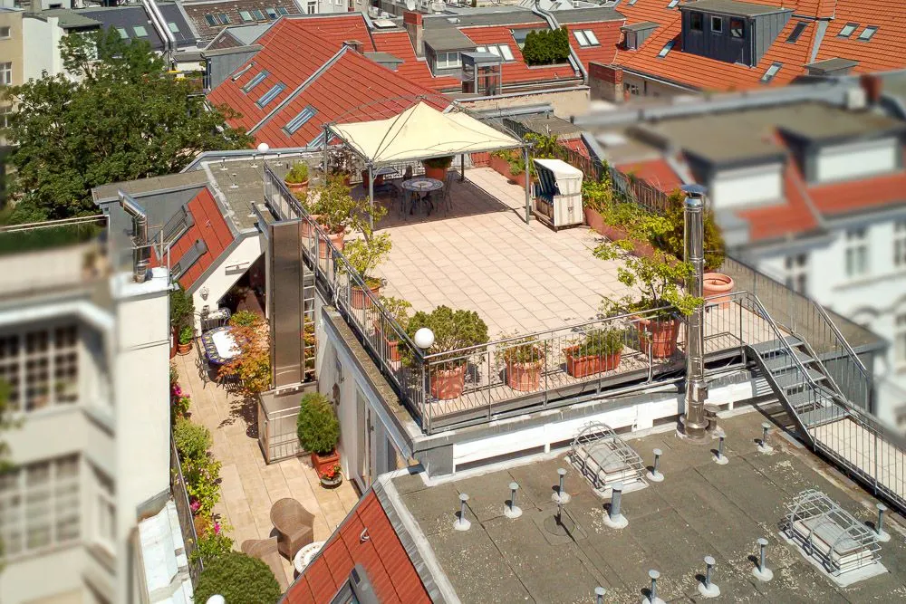 Dachterrasse mit Pavillon, Tisch, Stühlen und vielen Pflanzen in Töpfen.