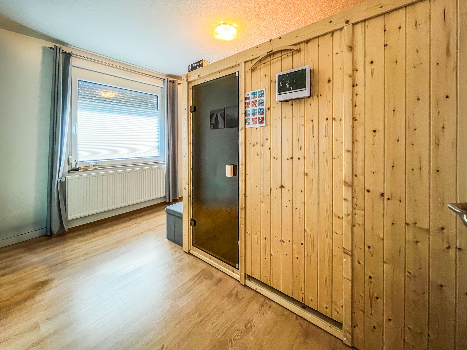 Holzsauna in einem Zimmer mit großem Fenster, Vorhängen und Holzboden.