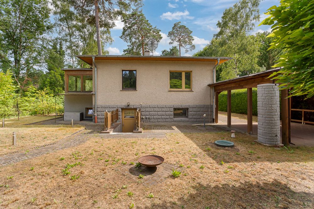 Rückseite eines Einfamilienhauses mit Garten, Terrasse und Carport, umgeben von Bäumen.