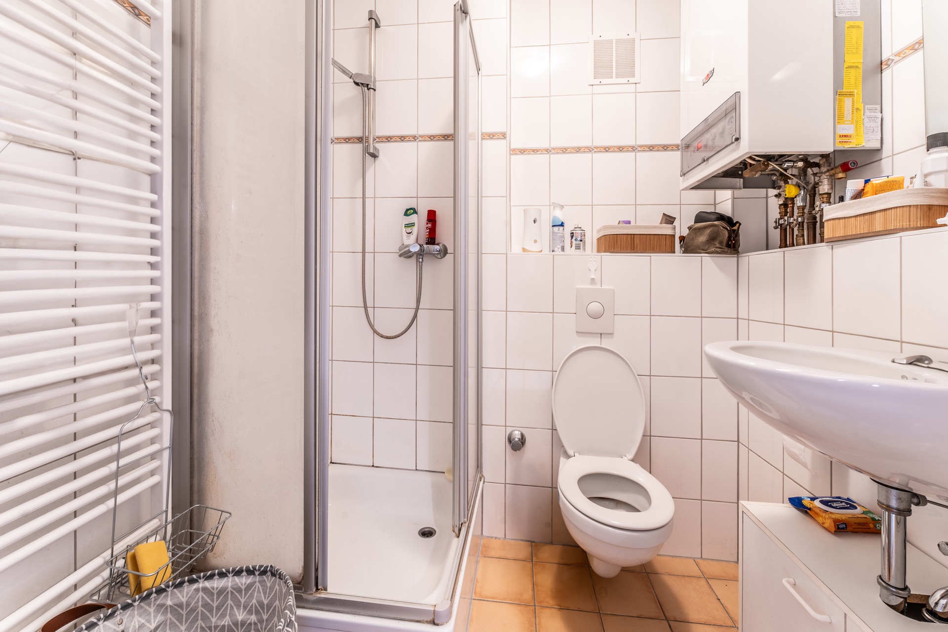 Badezimmer mit Dusche, Toilette, Waschbecken und Wandheizkörper, weiße Fliesen.