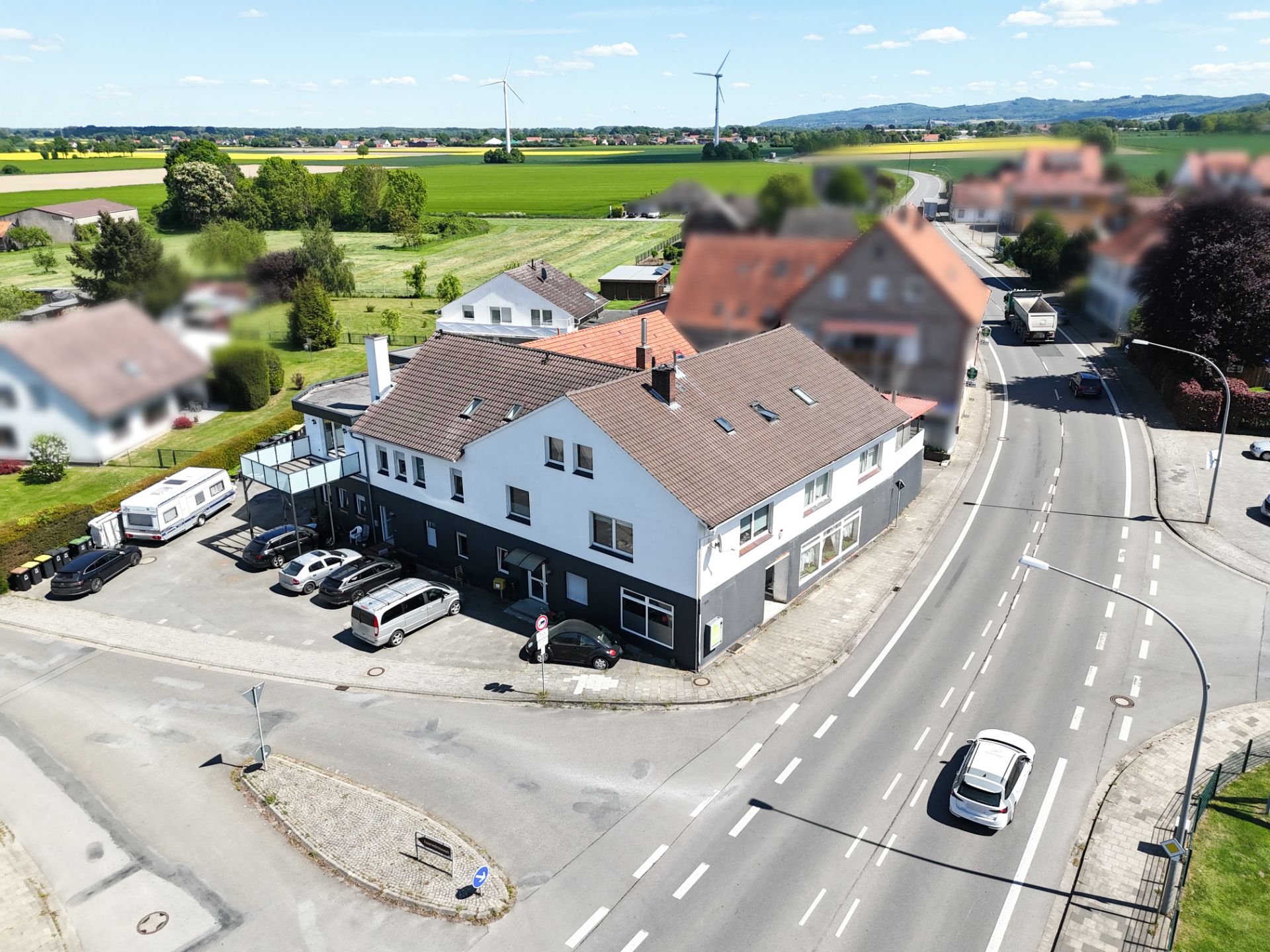 Eckhaus mit mehreren Autos auf dem Parkplatz, an einer Kreuzung in ländlicher Umgebung.