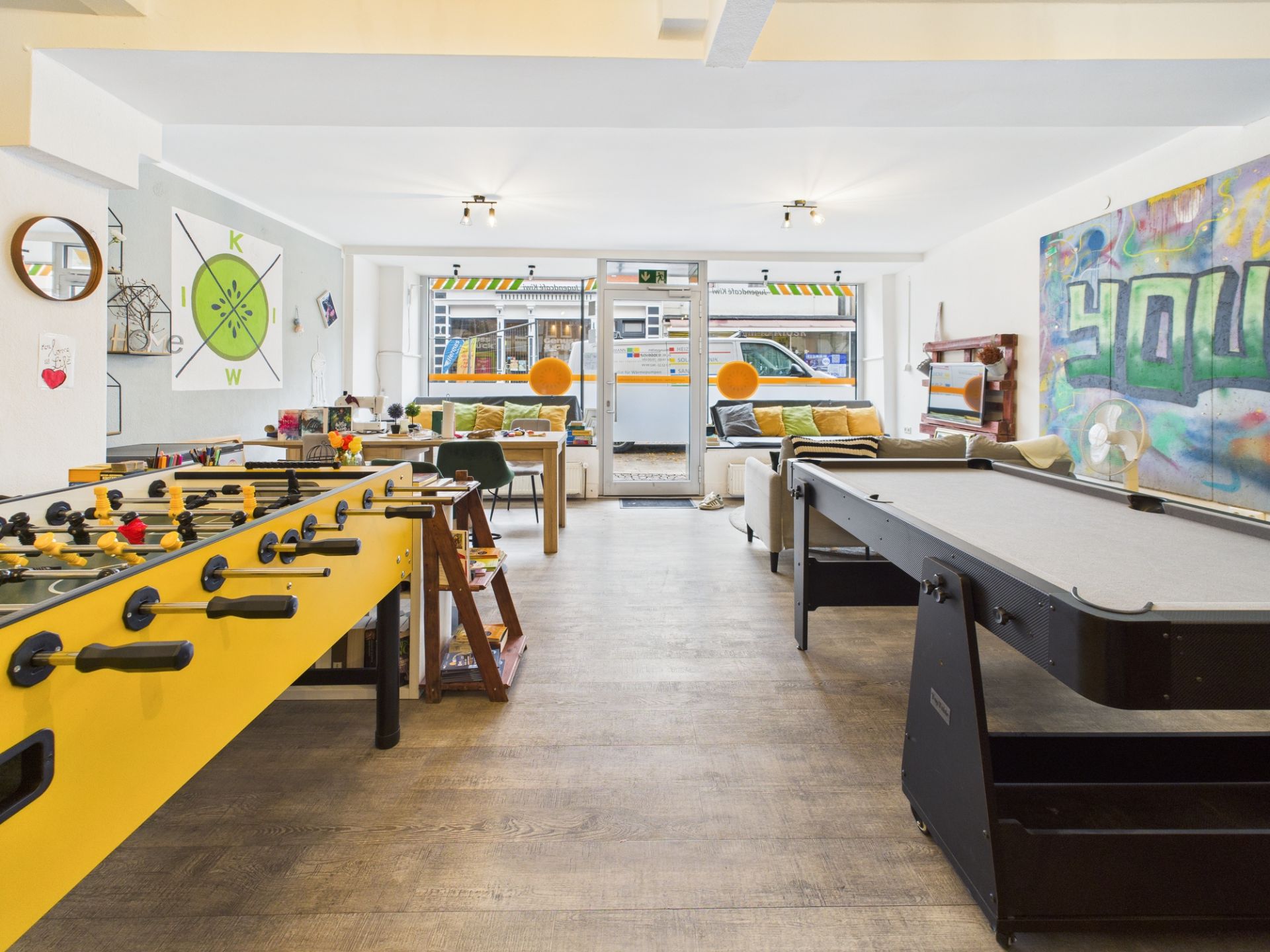 Heller Freizeitraum mit Kickertisch, Billardtisch, Sofas und bunter Wandgestaltung.