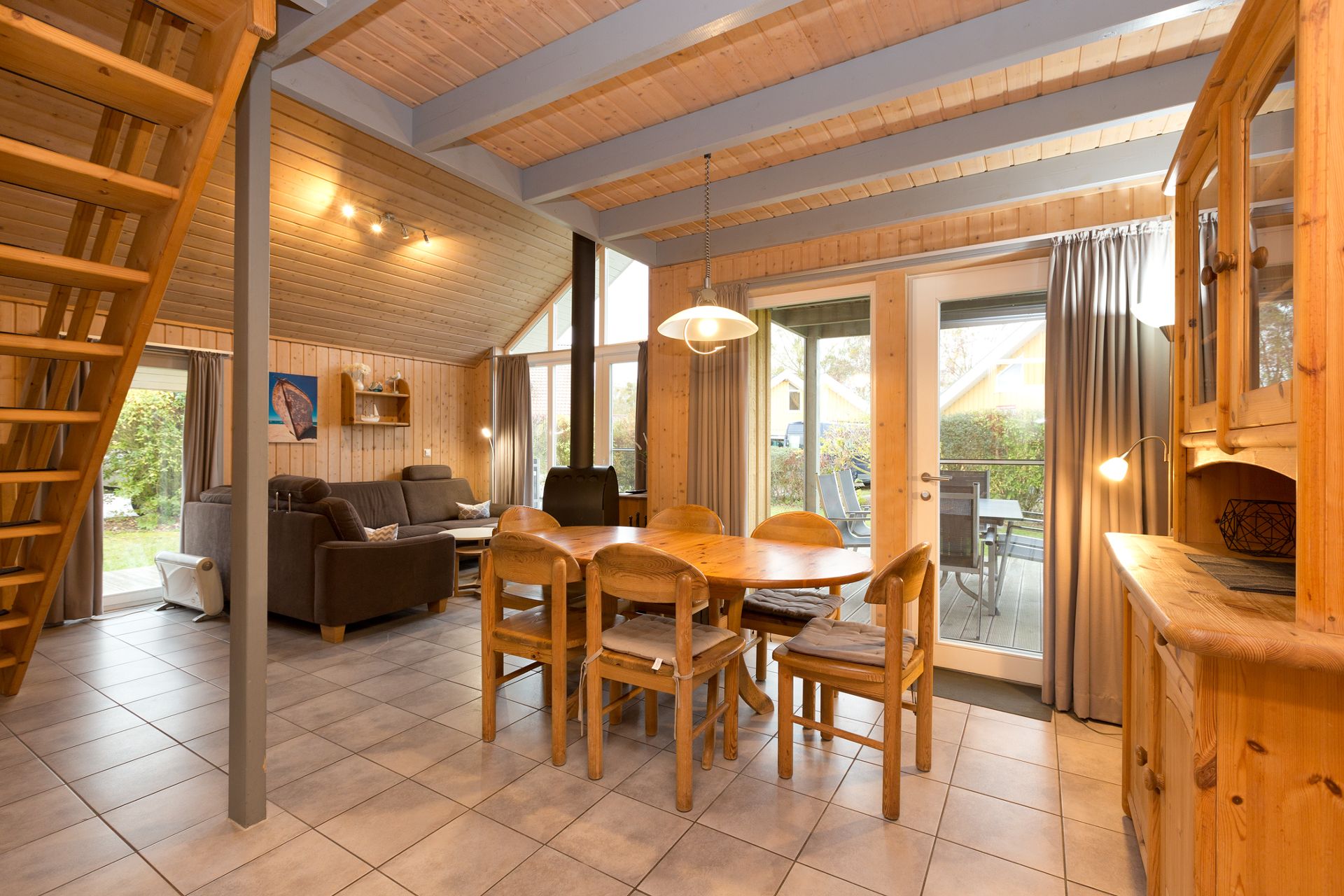 Wohnzimmer mit brauner Sitzgruppe, Esstisch, Holztreppe und Zugang zur Terrasse.