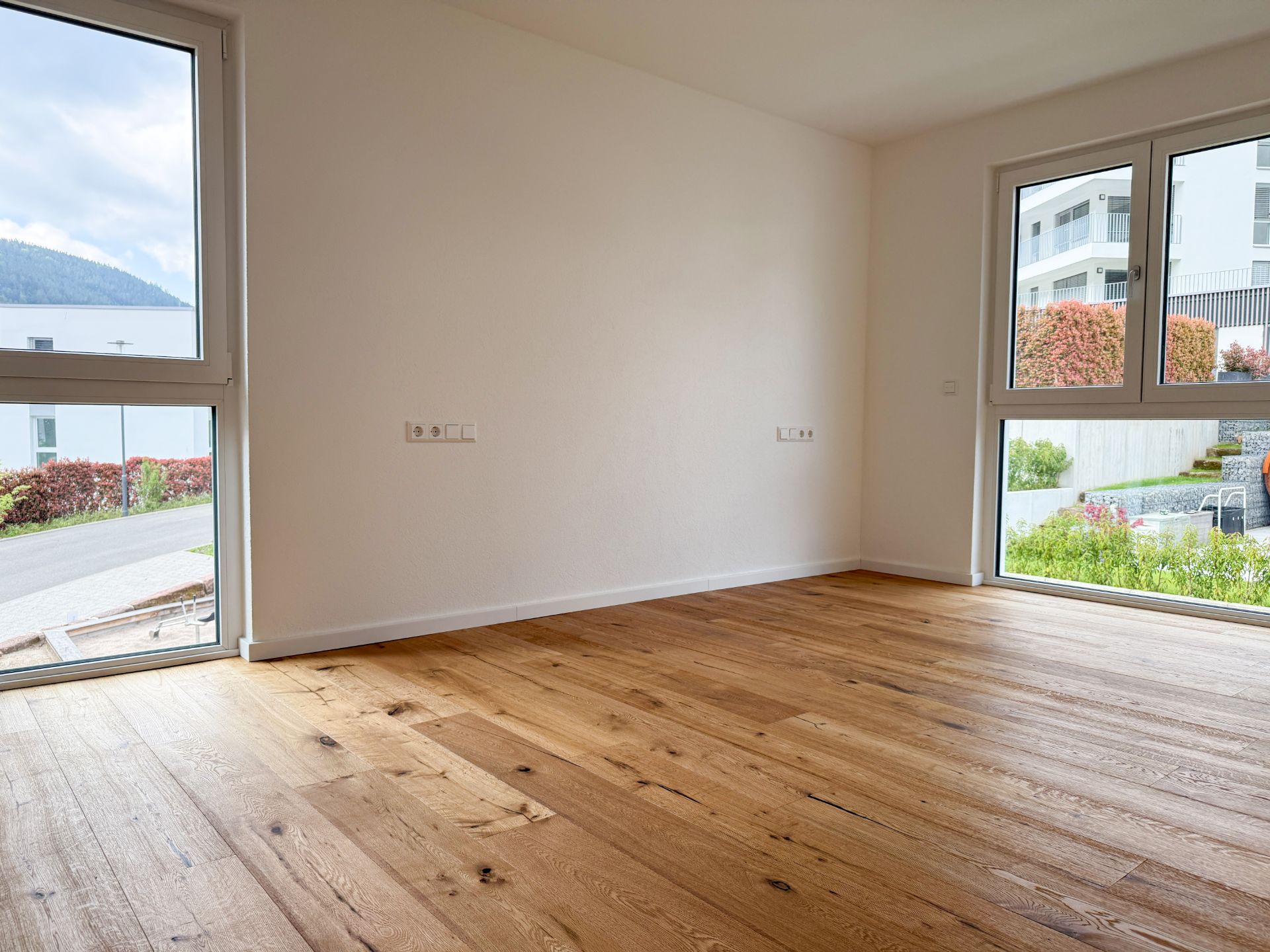 Leerer Raum mit Holzfußboden und großen Fenstern, Blick ins Freie.