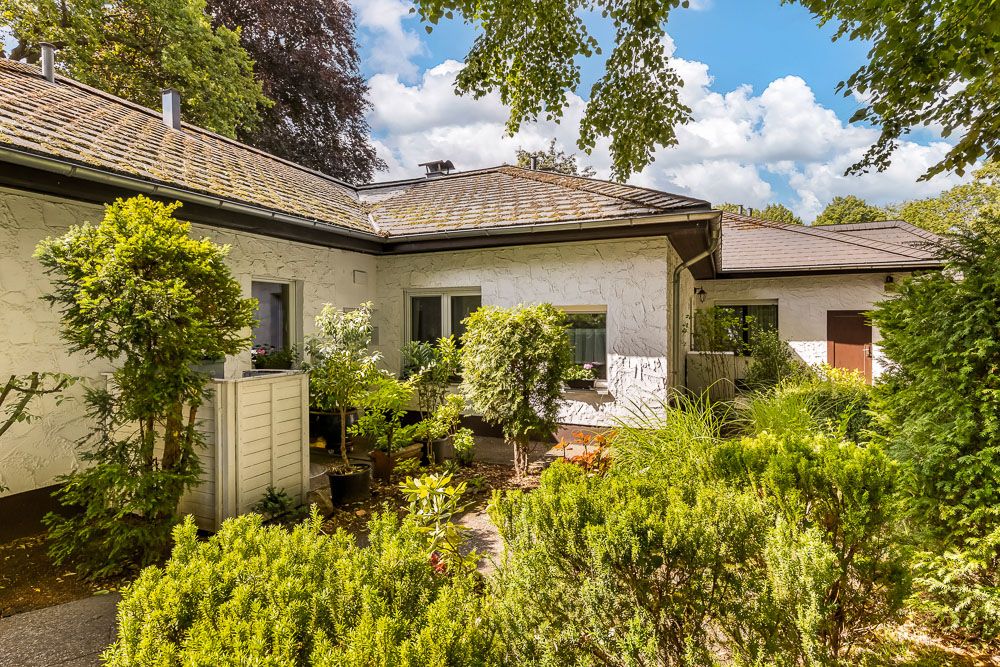 Einfamilienhaus mit hellem Putz, zwei Fenstern und grünem, bewachsenem Garten im Vordergrund.