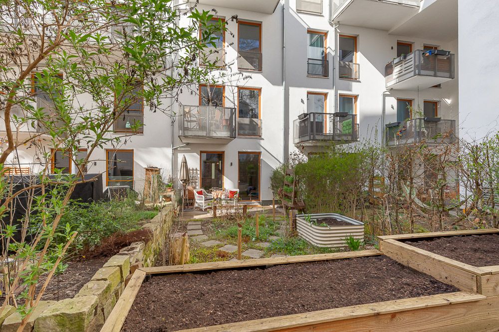 Gepflegter Hinterhof mit Hochbeeten, Pflanzen und Sitzbereich vor einem Wohnhaus mit Balkonen.