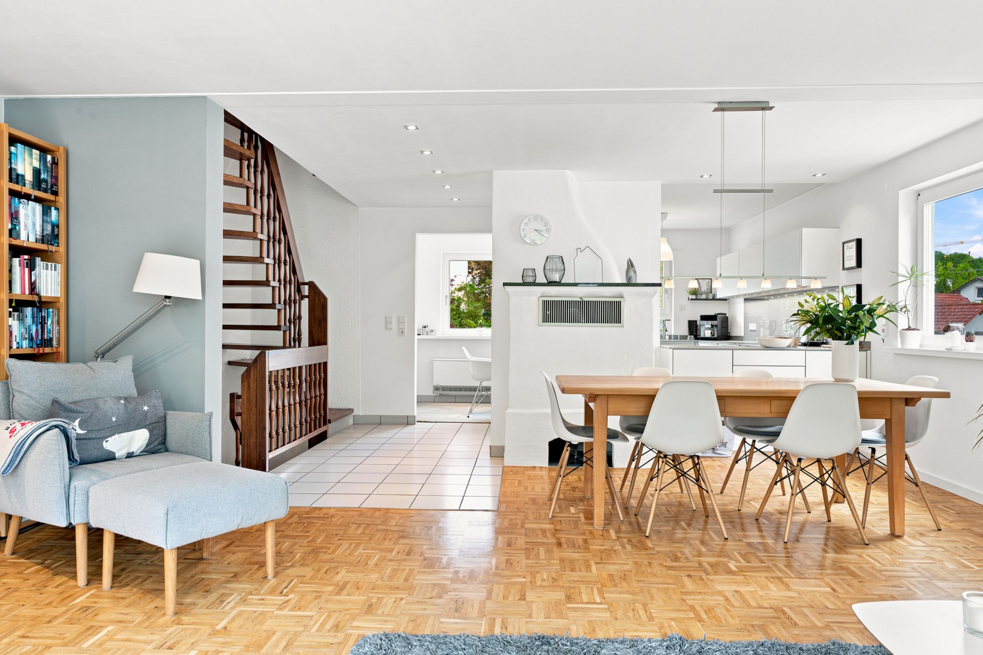 Helles Wohnzimmer mit Esstisch, Sessel, Bücherregal, Treppe und moderner Küche.
