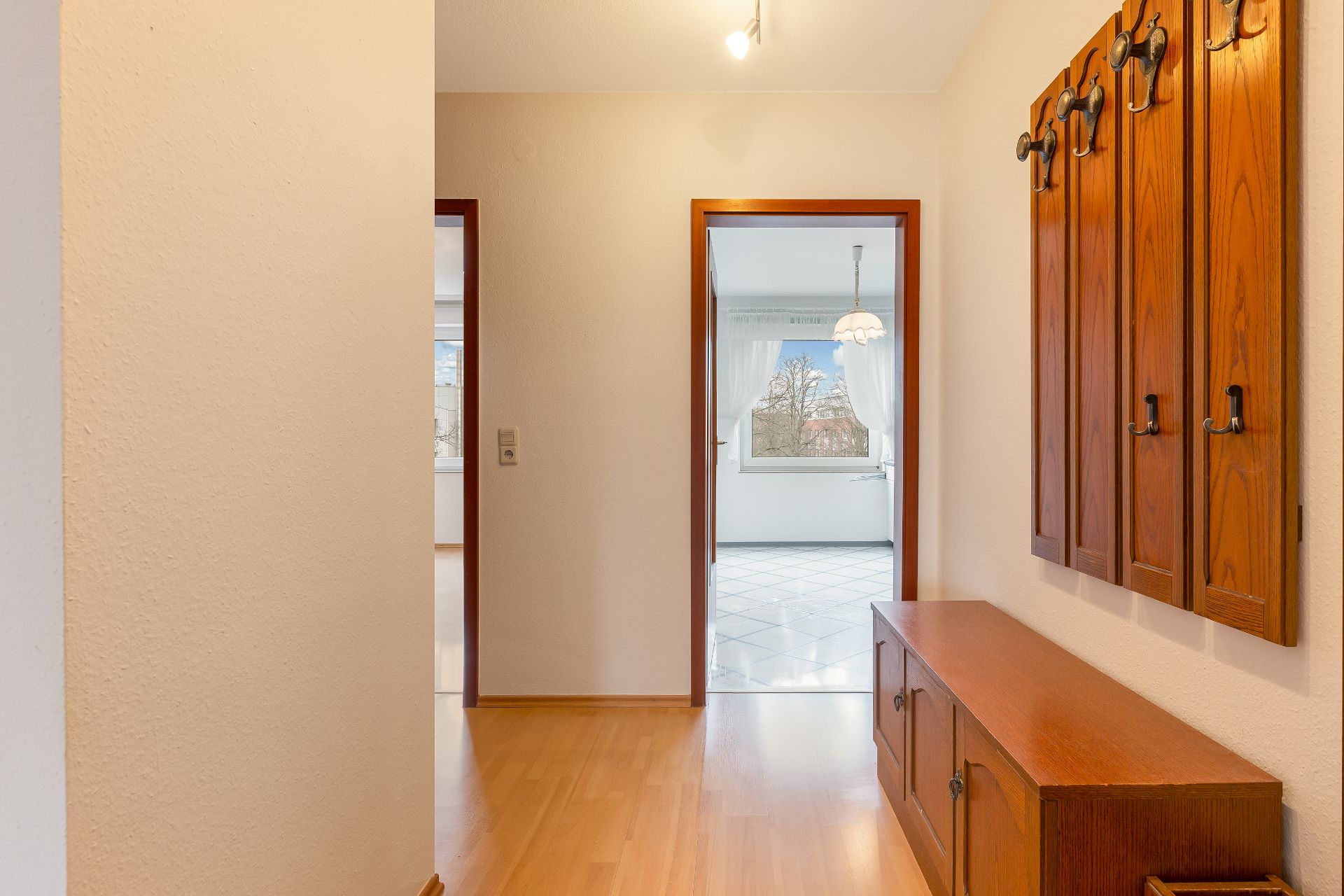 Flur mit Holzgarderobe, Holzboden und Blick in zwei helle, angrenzende Zimmer.