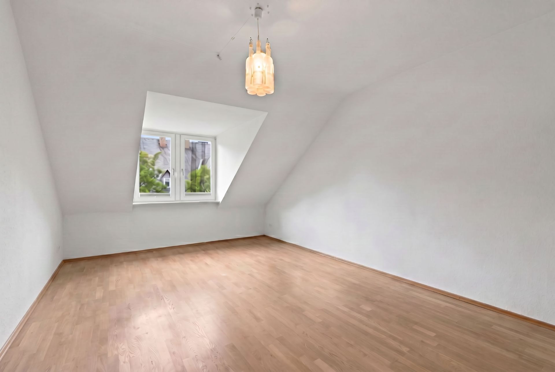 Leerer Raum mit Holzfußboden, weißem Wänden, Dachschräge und Fenster mit Ausblick.