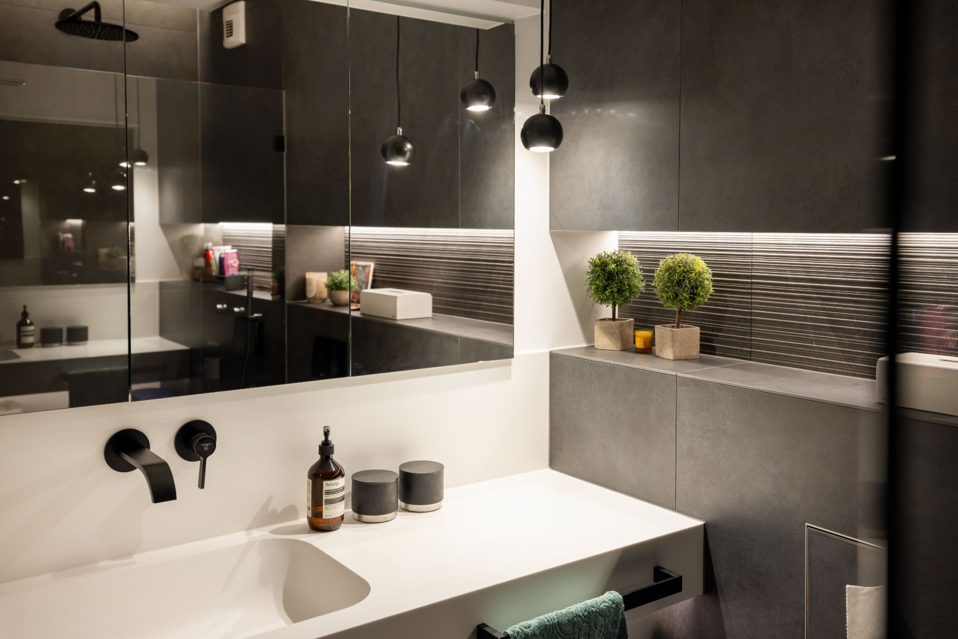 Modernes Badezimmer mit Waschbecken, Wandspiegel, Hängelampen und Dekopflanzen.