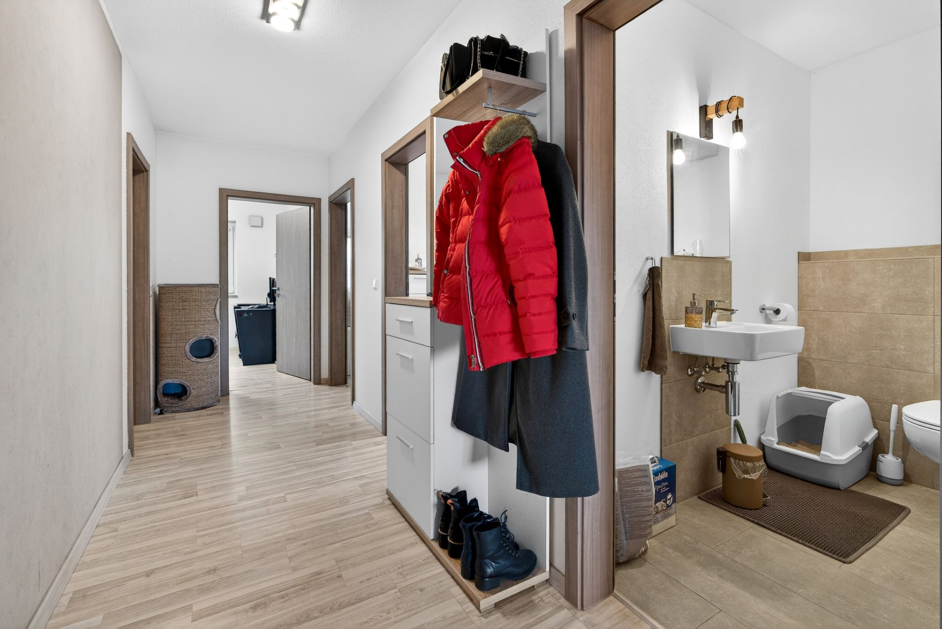 Heller Flur mit Garderobe, roten Jacken, Schuhen und Blick ins Badezimmer mit Katzenklo.