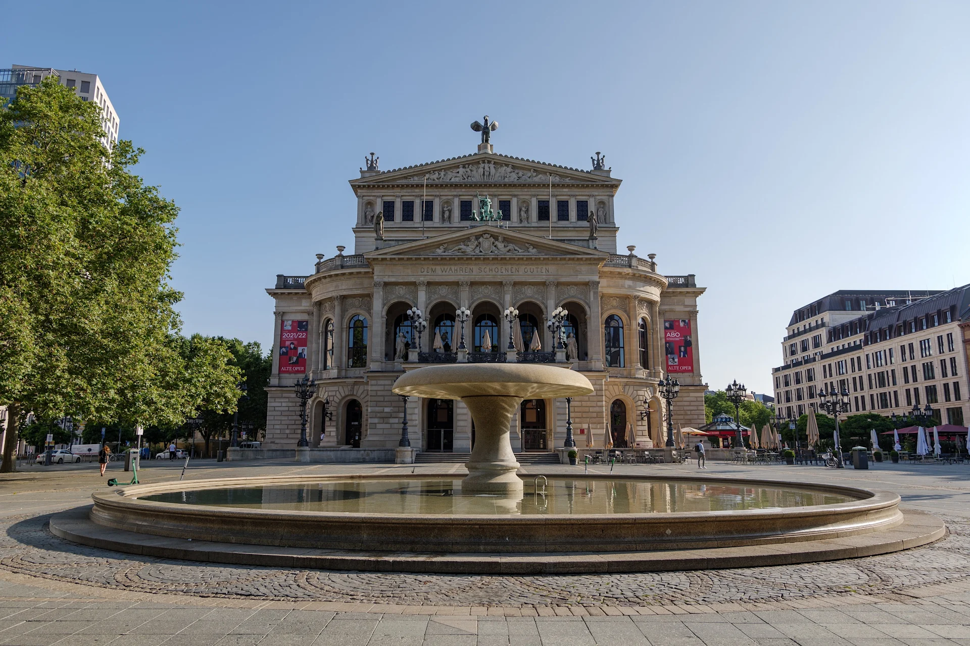 Großer Steinbrunnen auf einem Platz vor einem historischen Gebäude mit Statuen.