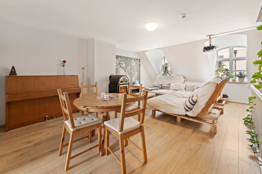 Helles Wohnzimmer mit Esstisch, Sofa, Klavier und Pflanzen auf Holzboden.
