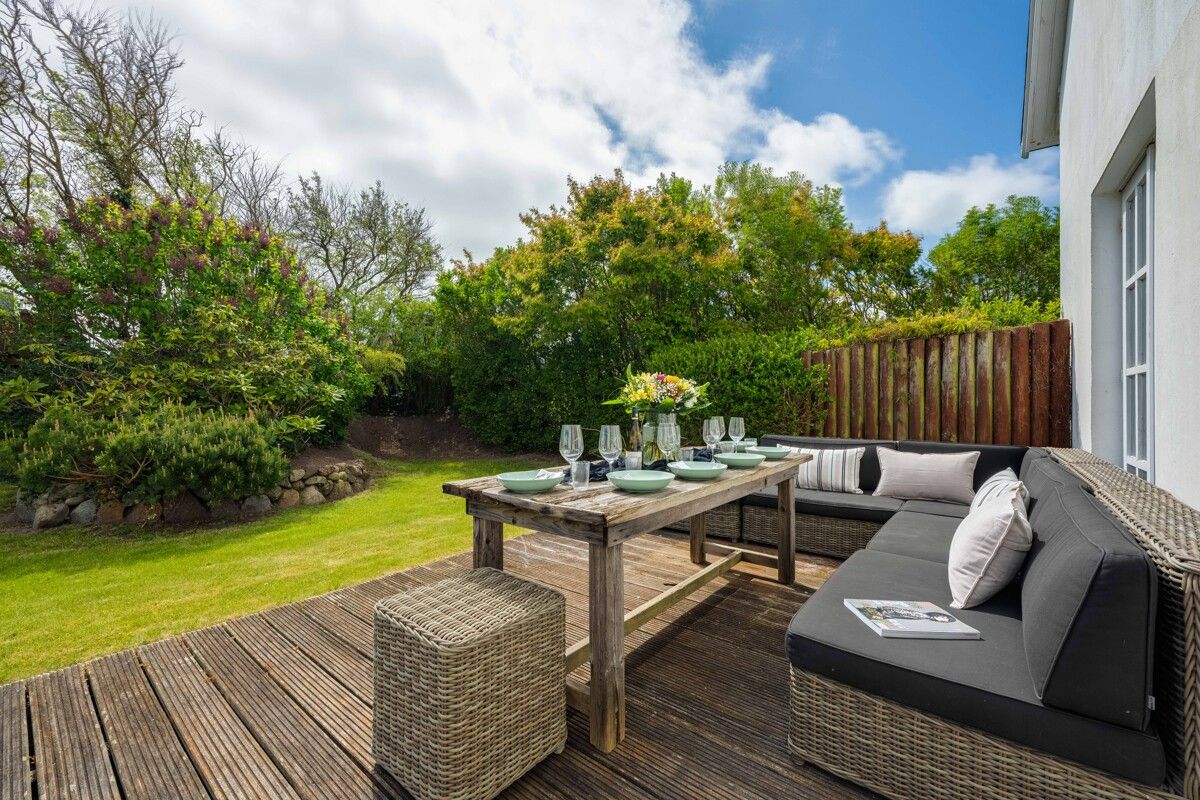 Holzterrasse mit Esstisch, Stühlen und Sofa, gedeckt für vier Personen, im Garten eines Wohnhauses.