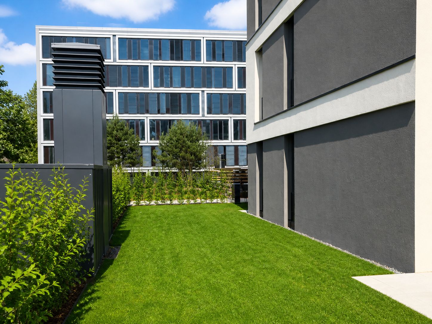 Grüner Garten neben einem modernen Wohngebäude mit Blick auf weitere Gebäude.