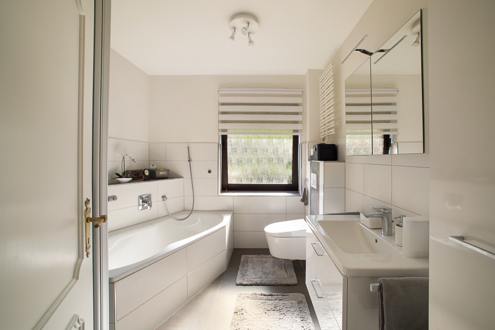 Modernes Badezimmer mit Badewanne, Waschbecken, WC und Fenster mit Jalousie.