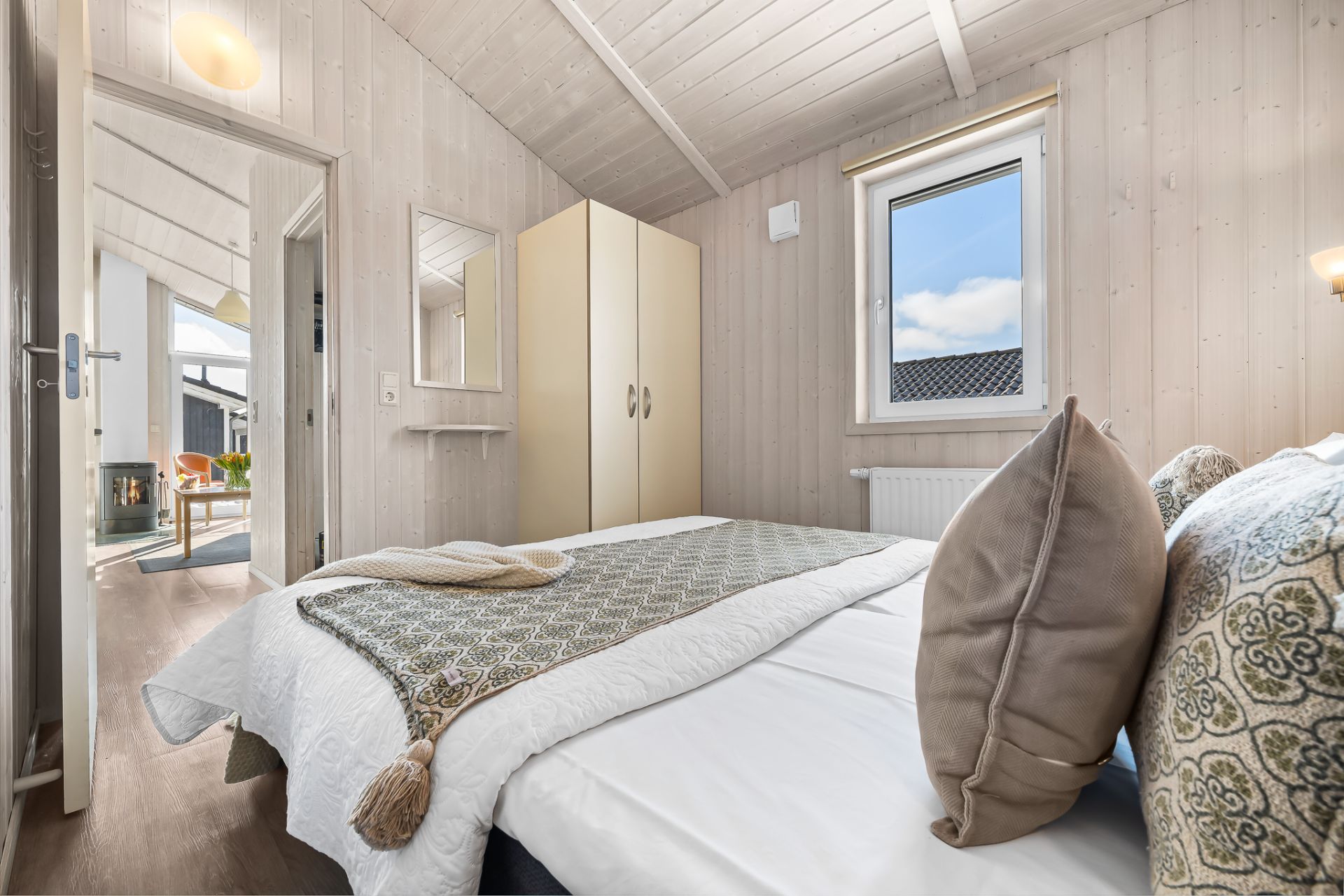 Helles Schlafzimmer mit Doppelbett, Kleiderschrank und Fenster, Holzwände und Decke.