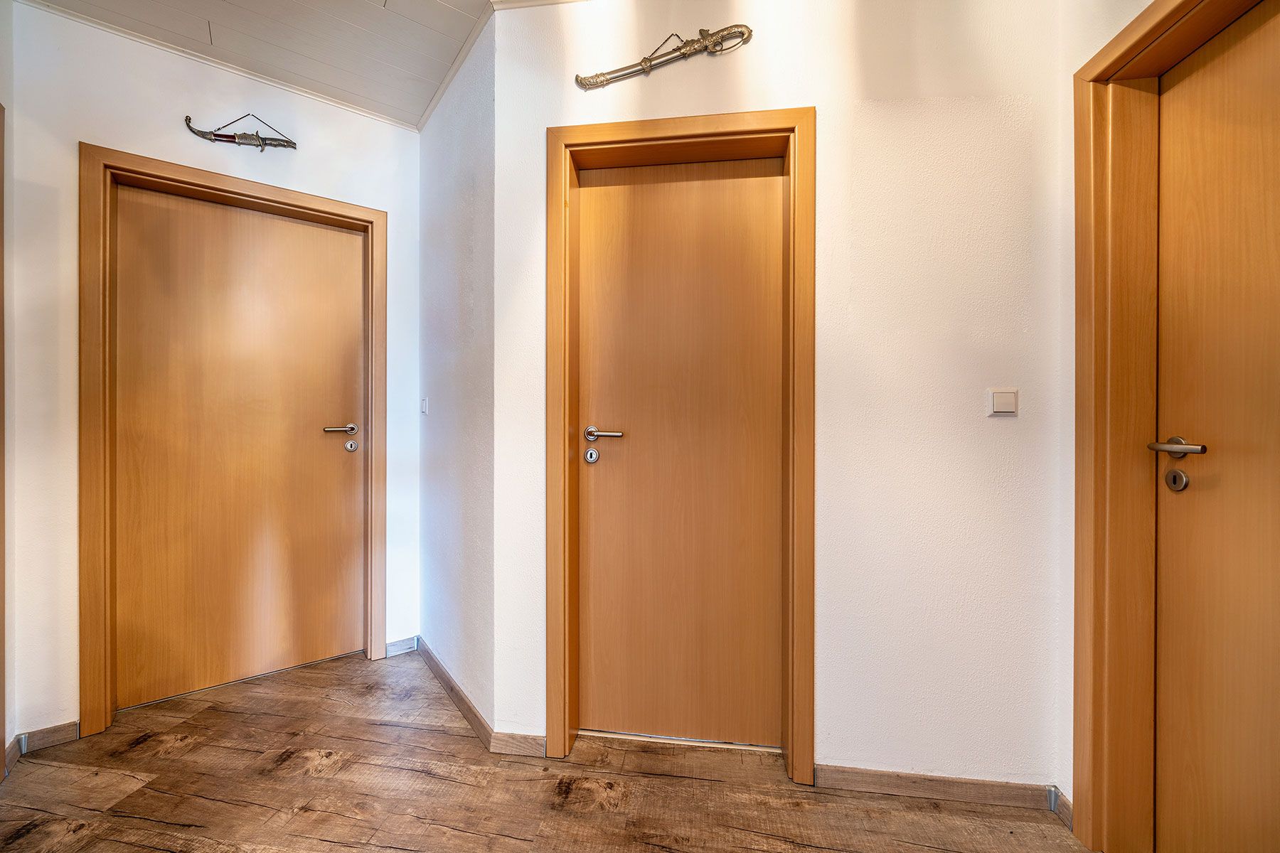 Flur mit drei Holztüren und Dekoration an der Wand, brauner Holzboden.
