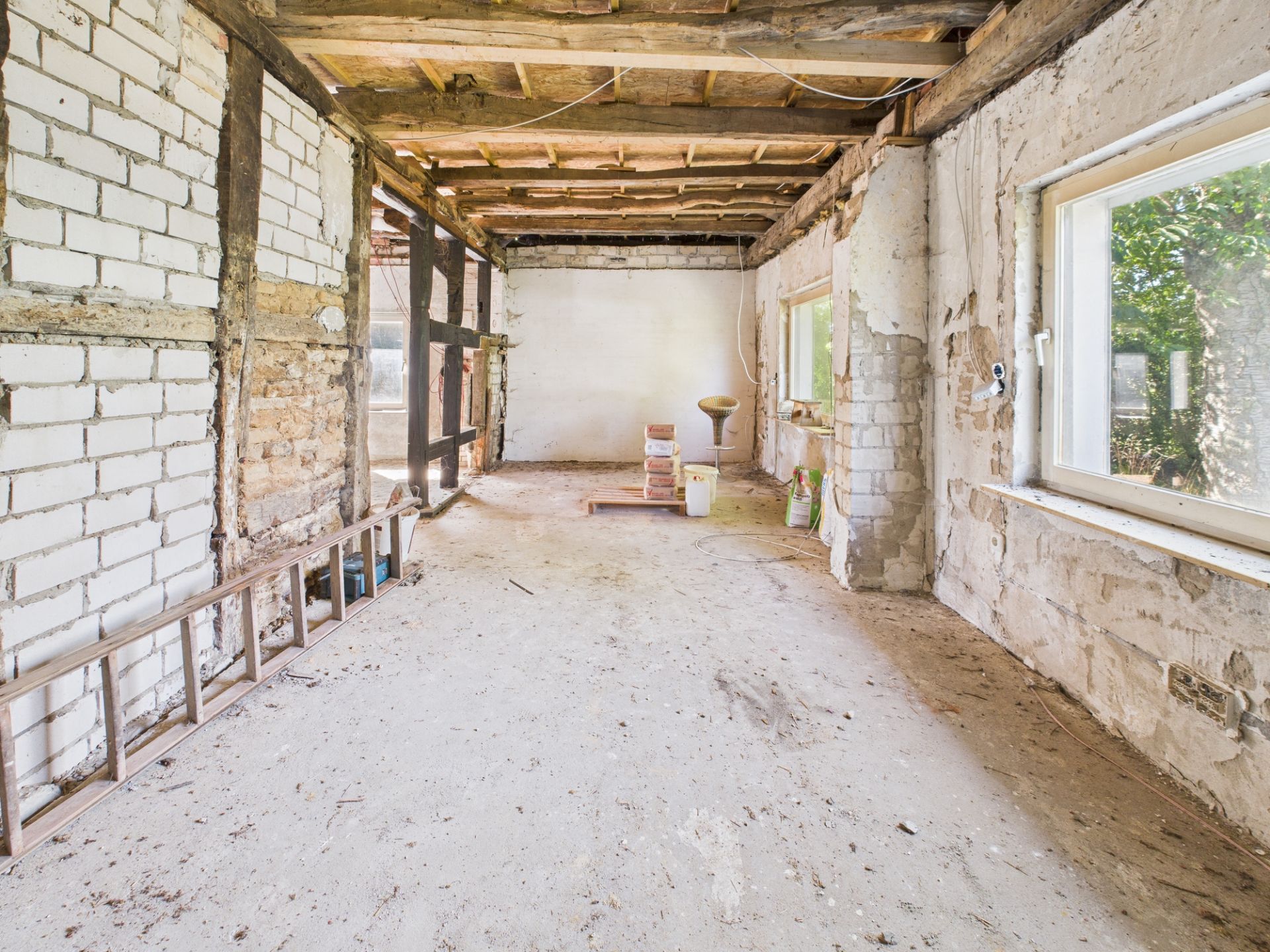 Leerer, renovierungsbedürftiger Raum mit unverputzten Wänden und sichtbarer Holzbalkendecke.