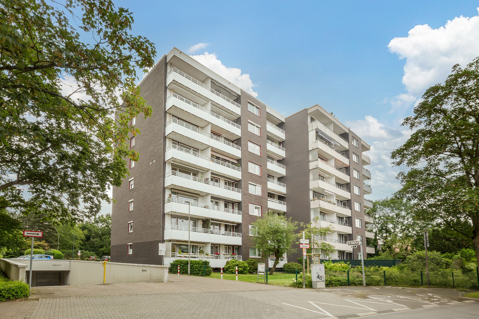 Mehrstöckiges Wohngebäude mit Balkonen und grüner Umgebung bei blauem Himmel.