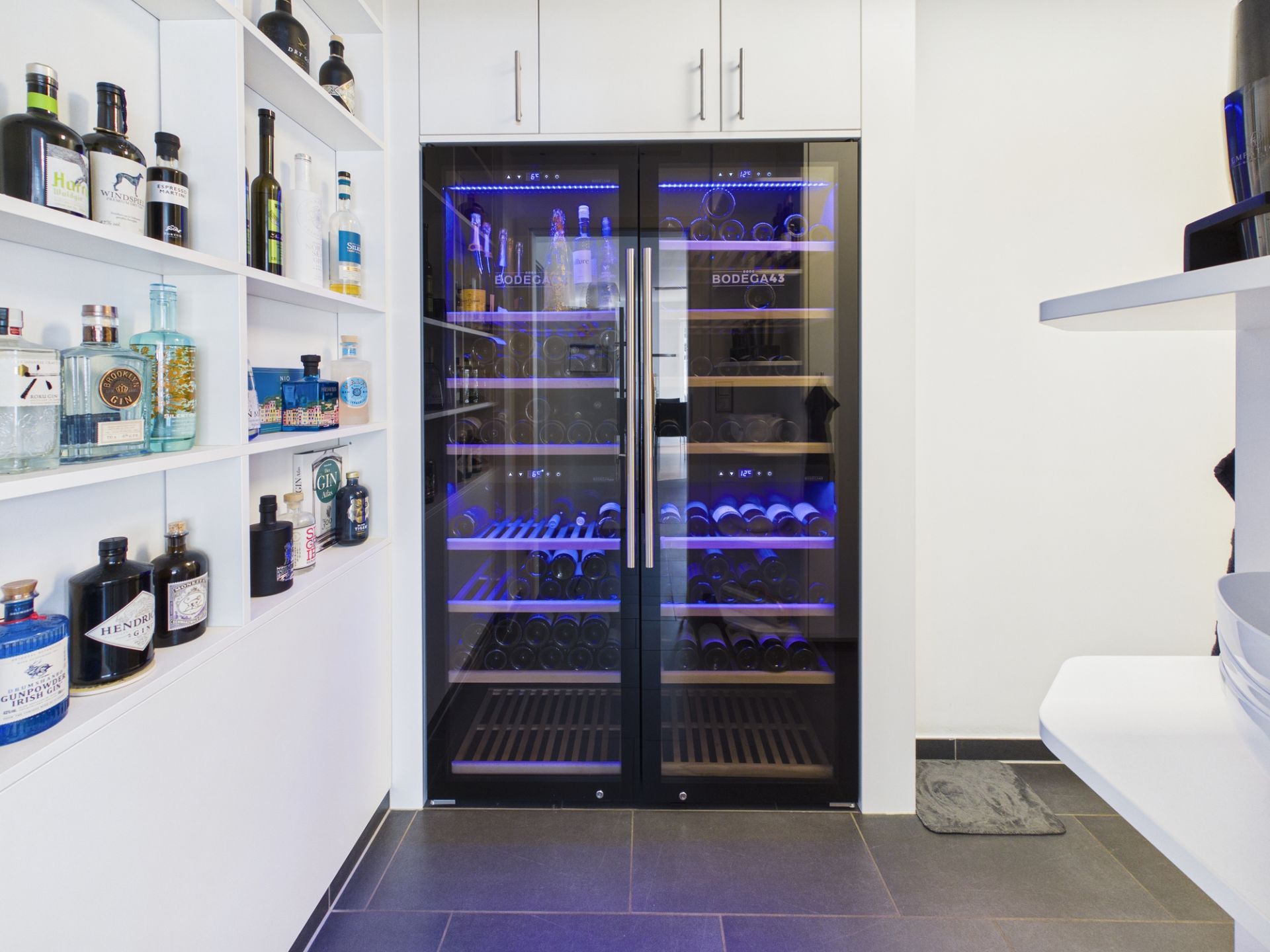 Weinkühlschrank mit Glasfront und beleuchteten Regalen, daneben ein Regal mit Flaschen.