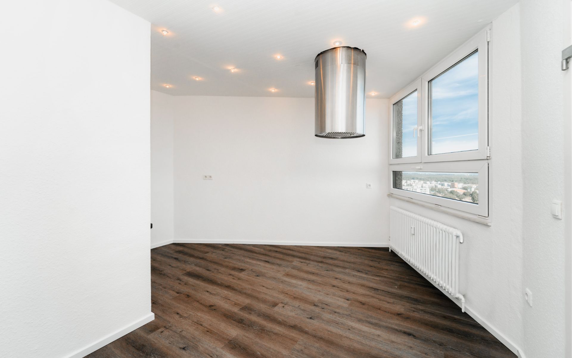 Heller Raum mit Holzfußboden, weißen Wänden, großem Fenster und Edelstahl-Dunstabzugshaube.
