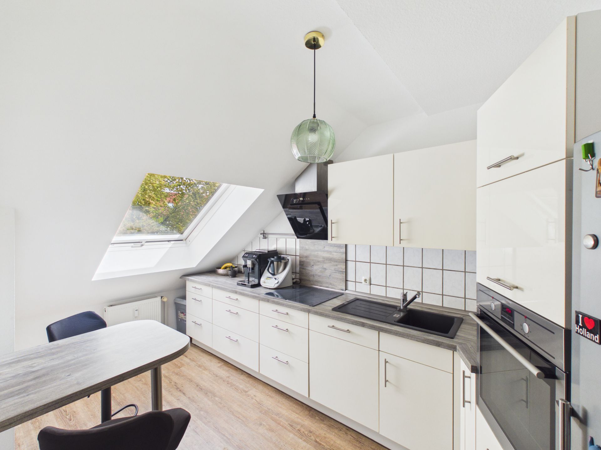 Helle Einbauküche mit Dachfenster, weißen Schränken und modernen Geräten.