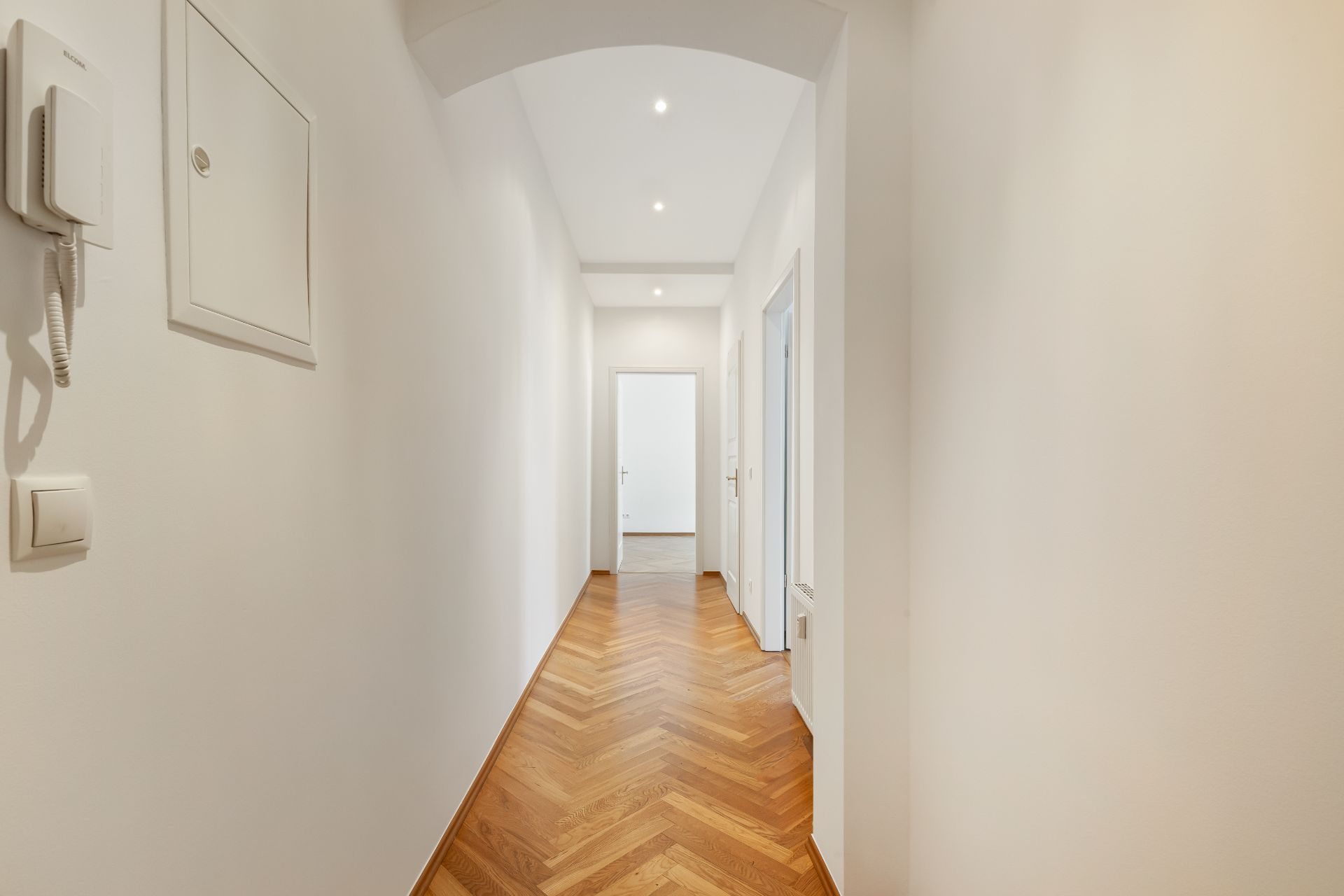 Langer, heller Flur mit Parkettboden und weißen Wänden in einer Wohnung.