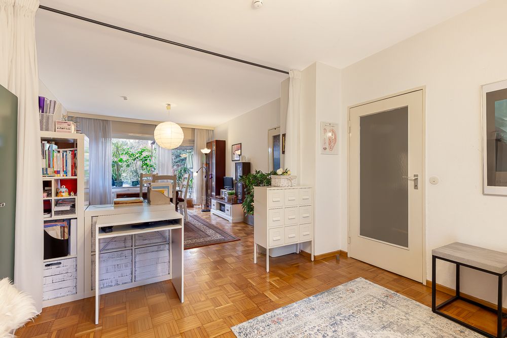Helles Wohnzimmer mit Schreibtisch, Bücherregal, Esstisch und großer Fensterfront zum Garten.