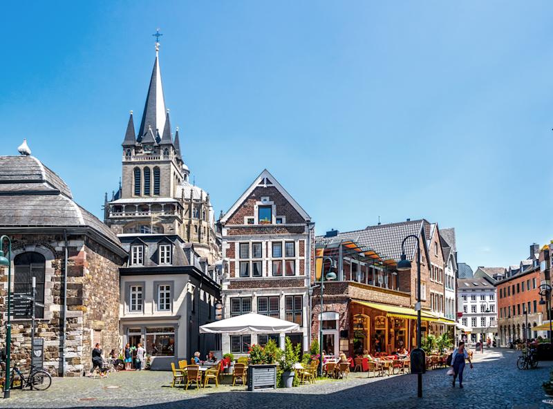 Historische Häuser mit Straßencafé und Menschen auf einem sonnigen Platz.