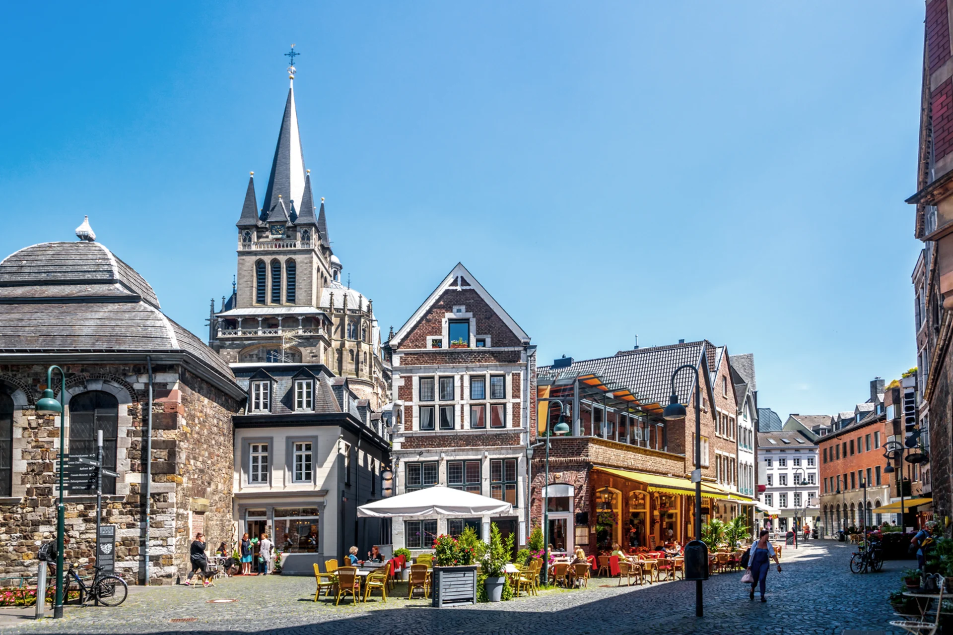 Historische Häuser mit Straßencafé und Menschen auf einem sonnigen Platz.