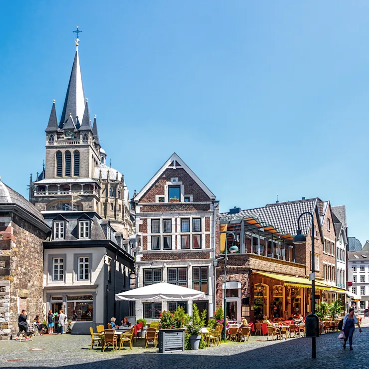 Historische Häuser mit Straßencafé und Menschen auf einem sonnigen Platz.
